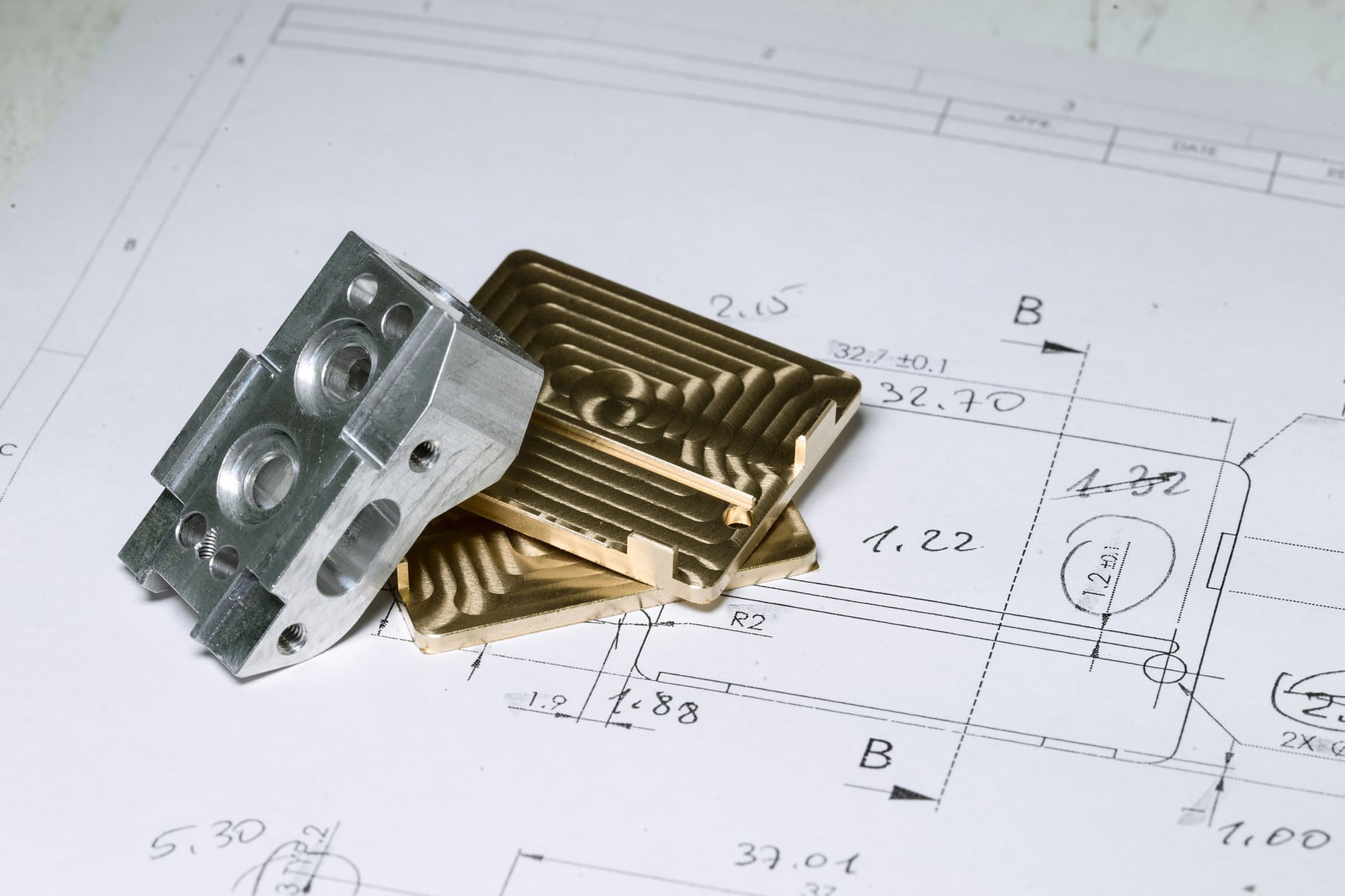 Gefräste Metallteile aus Aluminium und Messing auf der zugehörigen technischen Zeichnung